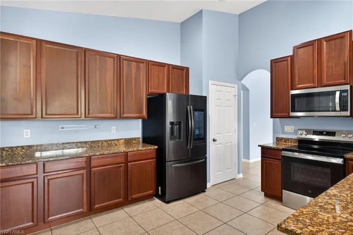 Kitchen with stainless steel appliances, dark stone countertops, arched walkways, a high ceiling, and light tile patterned flooring