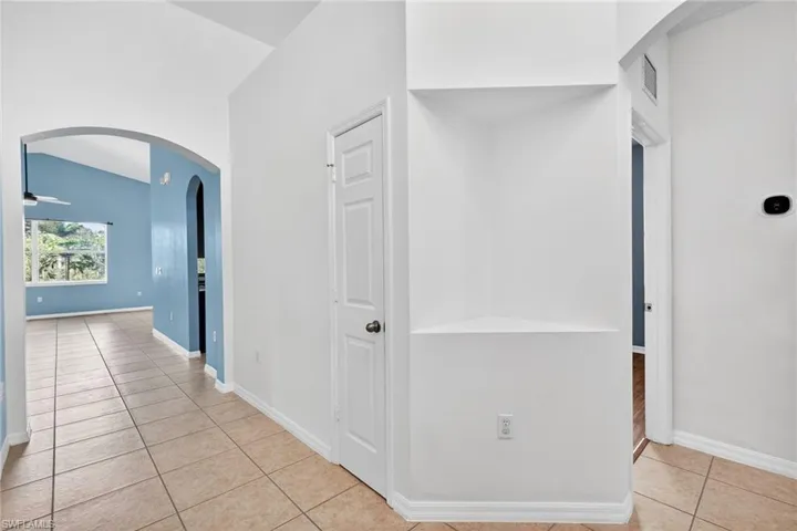 Corridor with arched walkways, light tile patterned flooring, and lofted ceiling