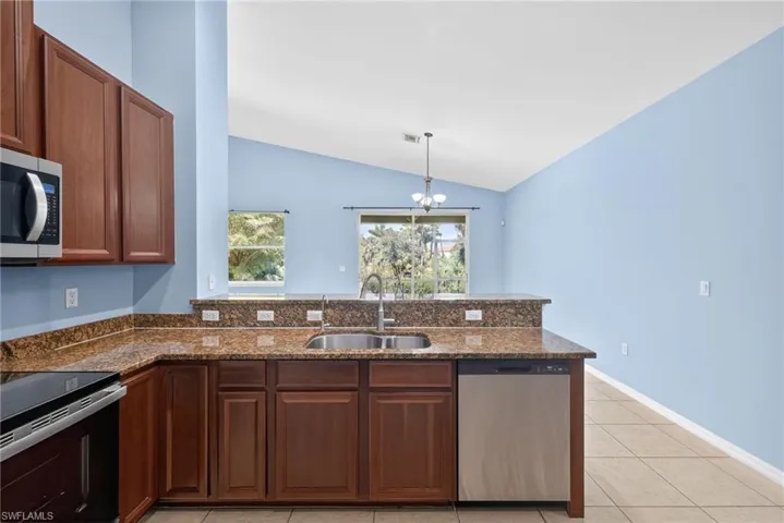Kitchen featuring a peninsula, stainless steel appliances, dark stone countertops, light tile patterned floors, and hanging light fixtures