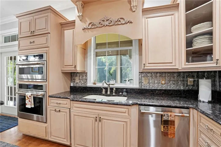 Kitchen with stainless steel appliances, dark stone countertops, backsplash, wood finished floors, and glass insert cabinets
