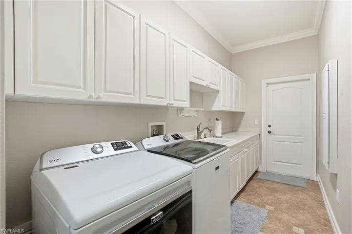 Laundry area with crown molding, washer and dryer, cabinet space, and light tile patterned flooring