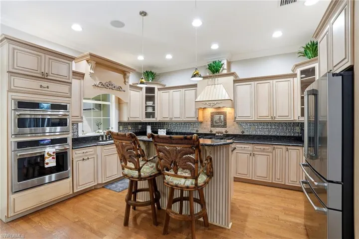 Kitchen with glass insert cabinets, stainless steel appliances, a breakfast bar area, backsplash, and dark stone countertops