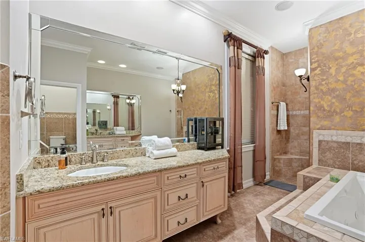 Bathroom featuring crown molding, a garden tub, vanity, light tile patterned flooring, and a chandelier