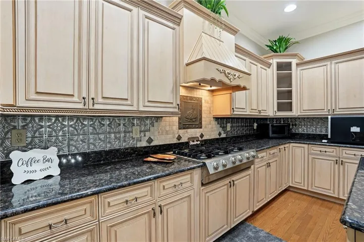 Kitchen with light wood finished floors, tasteful backsplash, stainless steel gas stovetop, dark stone countertops, and cream cabinetry