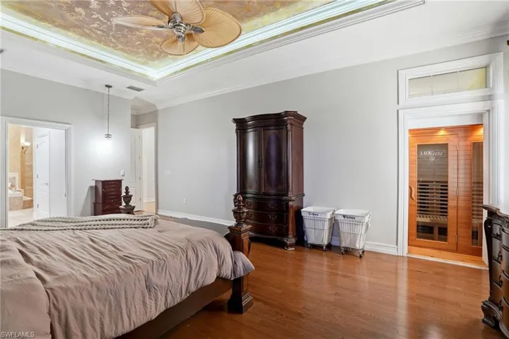 Bedroom with ornamental molding, wood finished floors, ensuite bath, a ceiling fan, and a raised ceiling