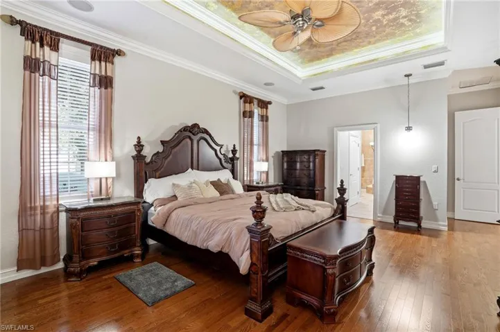 Bedroom featuring a raised ceiling, crown molding, wood-type flooring, ceiling fan, and ensuite bathroom