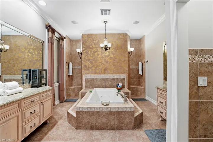 Full bath with a chandelier, vanity, a jetted tub, crown molding, and tile walls