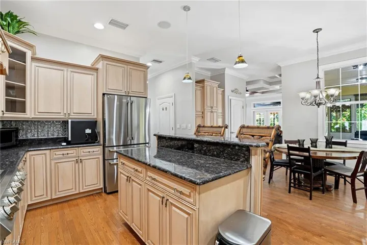 Kitchen with pendant lighting, glass insert cabinets, ornamental molding, high end fridge, and dark stone countertops