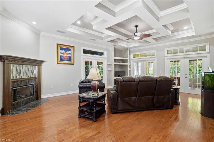 Living room with a premium fireplace, french doors, light wood finished floors, ornamental molding, and coffered ceiling