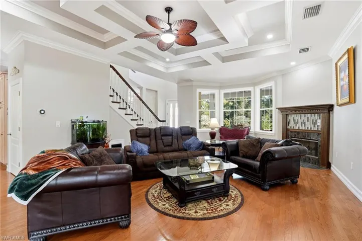 Living area with coffered ceiling, light wood-style floors, a ceiling fan, beamed ceiling, and ornamental molding