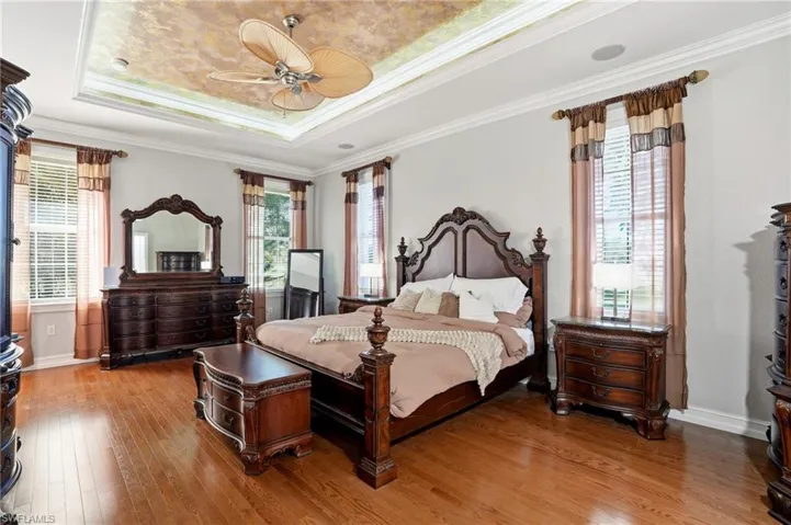 Bedroom with a raised ceiling, ornamental molding, light wood-style flooring, and multiple windows