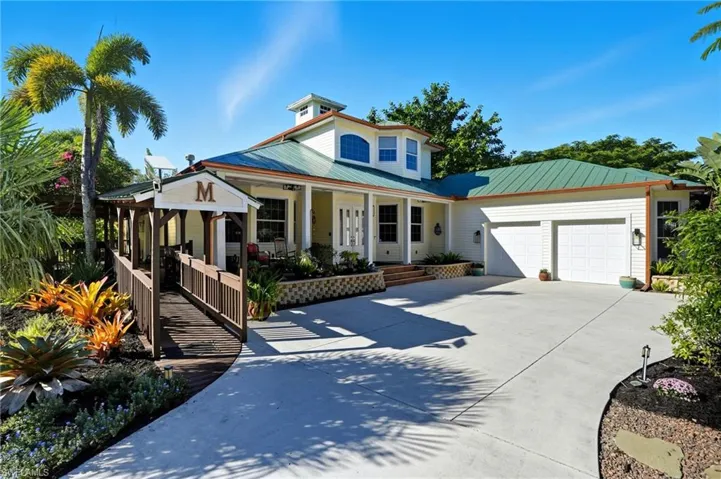 View of front of house with covered porch, driveway, a garage, and a metal roof