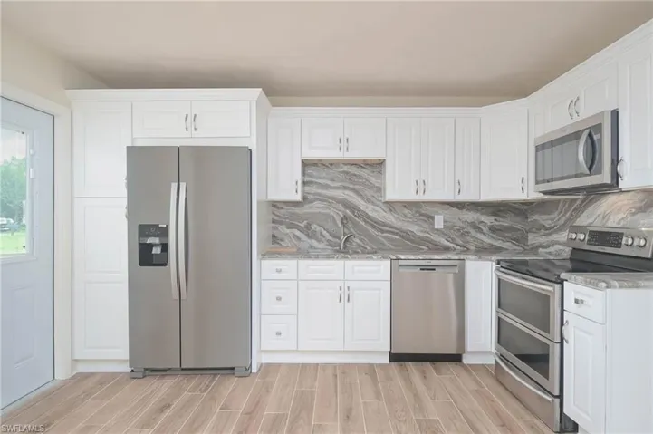 Kitchen featuring white cabinets, light wood-type flooring, light stone counters, stainless steel appliances, and ceiling fan