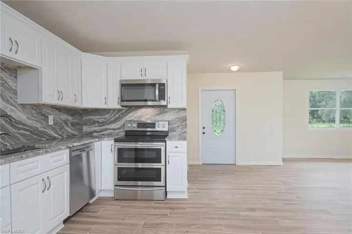 Kitchen featuring white cabinets, appliances with stainless steel finishes, light hardwood / wood-style floors, and stone counters