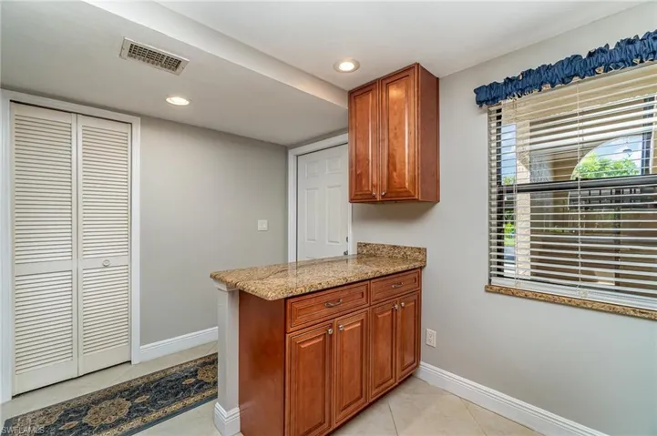 Kitchen with light stone counters, a peninsula, brown cabinets, recessed lighting, and light tile patterned floors