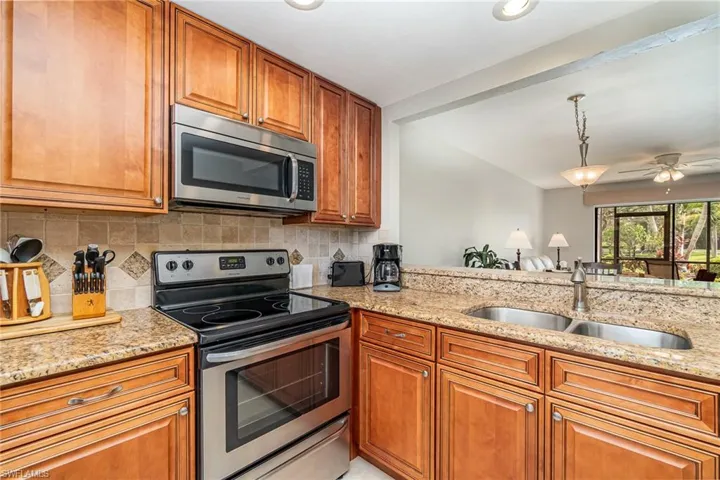 Kitchen with stainless steel appliances, brown cabinetry, light stone countertops, hanging light fixtures, and tasteful backsplash