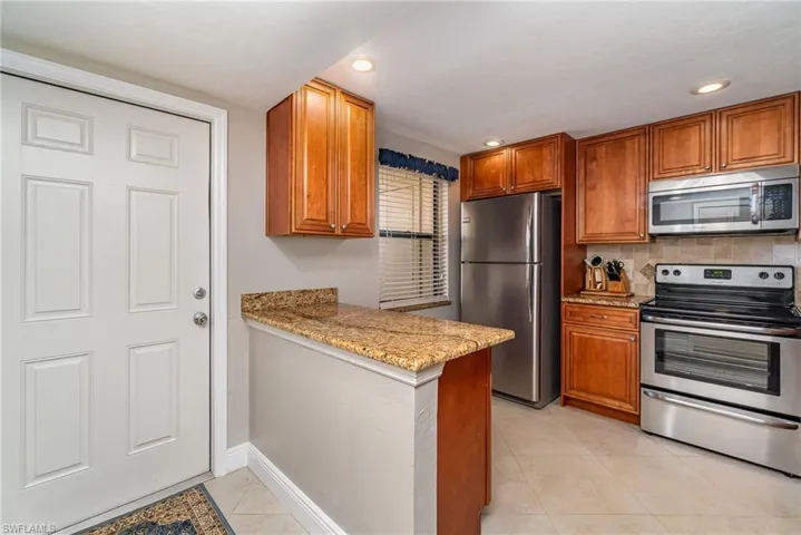 Kitchen featuring appliances with stainless steel finishes, brown cabinets, light stone countertops, light tile patterned floors, and a peninsula