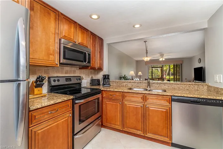 Kitchen with stainless steel appliances, brown cabinets, light stone countertops, and recessed lighting