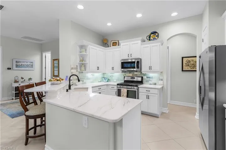 Kitchen with a peninsula, appliances with stainless steel finishes, open shelves, a kitchen breakfast bar, and white cabinets