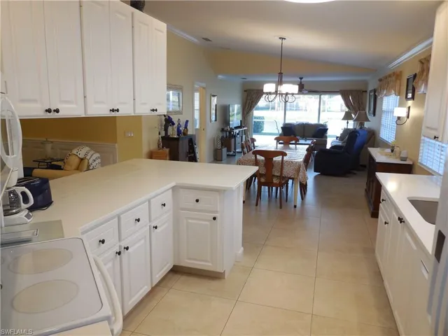 Kitchen with kitchen peninsula, light tile patterned floors, pendant lighting, white cabinetry, and an inviting chandelier
