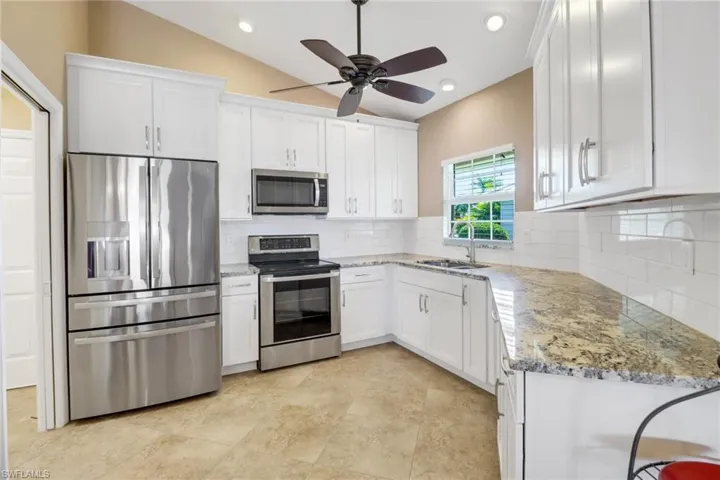 Kitchen with sink, white cabinetry, vaulted ceiling, stainless steel appliances, and backsplash