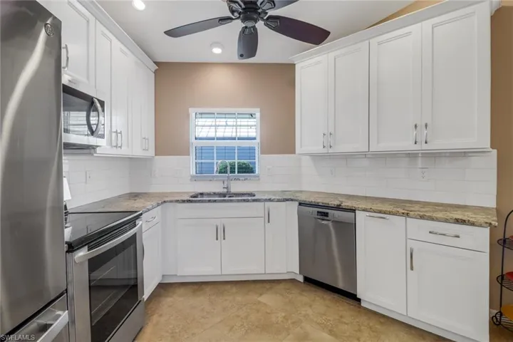 Kitchen featuring sink, light stone countertops, white cabinets, and appliances with stainless steel finishes