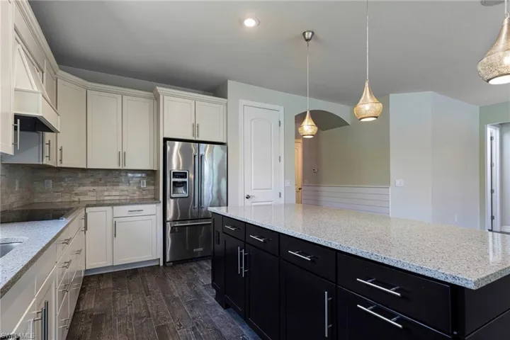 Kitchen featuring premium range hood, high end refrigerator, tasteful backsplash, pendant lighting, and wood-type flooring