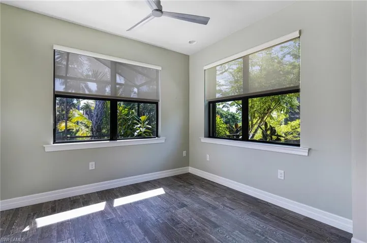 Spare room with ceiling fan, plenty of natural light, and dark hardwood / wood-style floors
