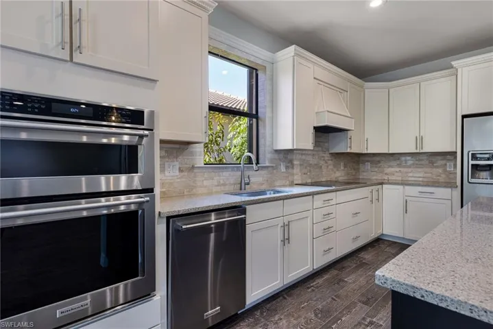Kitchen with appliances with stainless steel finishes, dark wood-type flooring, decorative backsplash, and custom range hood