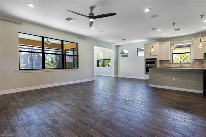 Unfurnished living room with ceiling fan, sink, dark wood-type flooring, and a healthy amount of sunlight