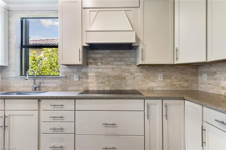 Kitchen with backsplash, black electric cooktop, stone counters, sink, and custom exhaust hood
