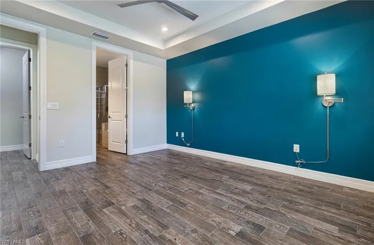 Empty room with dark hardwood / wood-style flooring, a raised ceiling, and ceiling fan