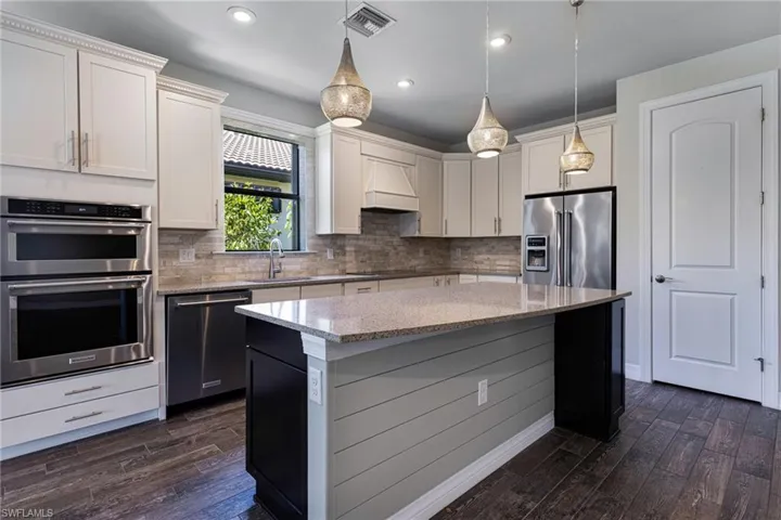 Kitchen featuring backsplash, stainless steel appliances, dark hardwood / wood-style floors, light stone counters, and a center island