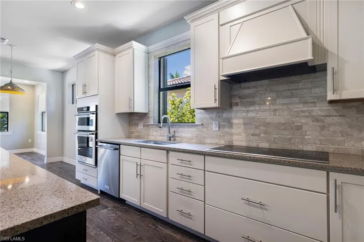 Kitchen featuring custom range hood, stainless steel appliances, tasteful backsplash, sink, and dark wood-type flooring