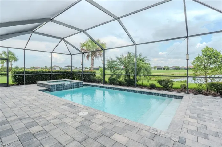 Screened pool enclosure featuring a rectangular pool with integrated spa, paver deck, and lush landscaping