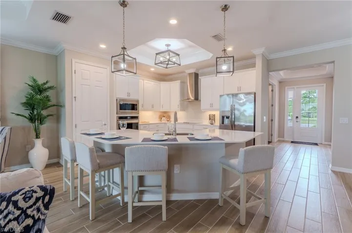 Open-concept kitchen featuring an oversized island with seating, white cabinetry, stainless steel appliances, and pendant lighting