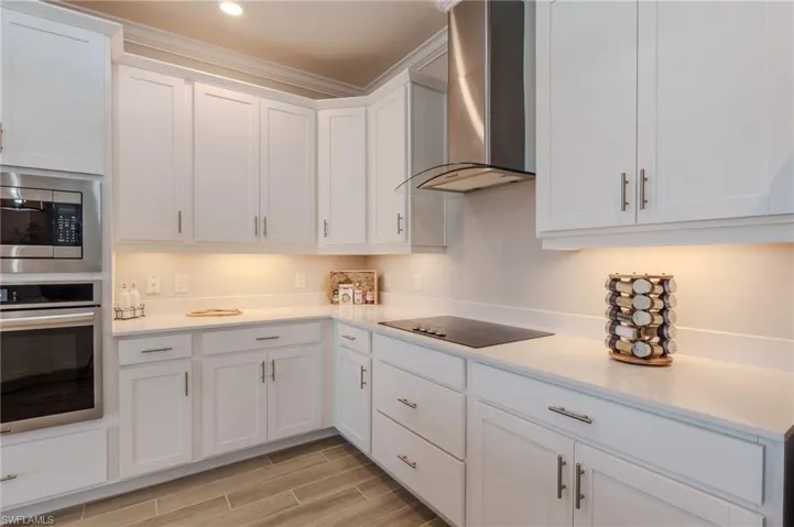 Kitchen featuring white cabinetry, light countertops, stainless steel appliances, a built-in oven, and wood-finish flooring