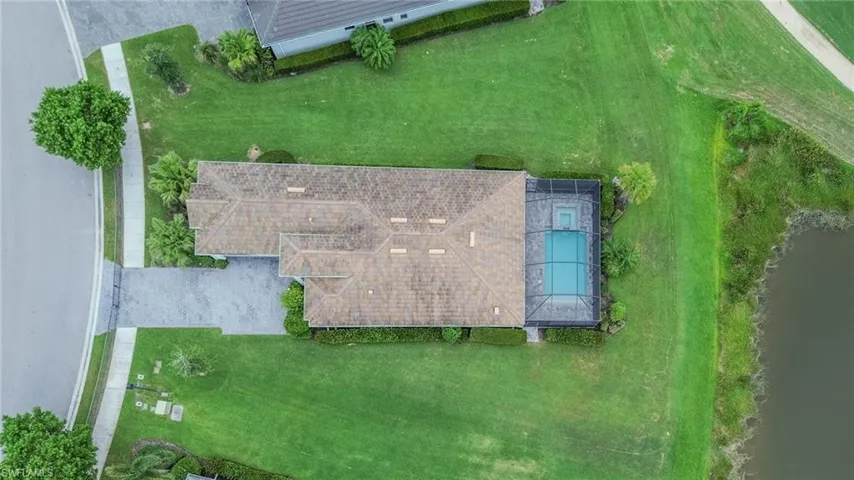 Aerial perspective showcasing a sprawling property featuring extensive green lawns, a paved driveway, and a screened swimming pool with an integrated spa