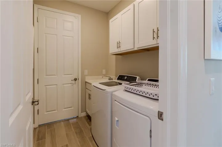 Utility room featuring wood-finish flooring, white cabinetry, a built-in countertop with an undermount sink, and neutral wall tones