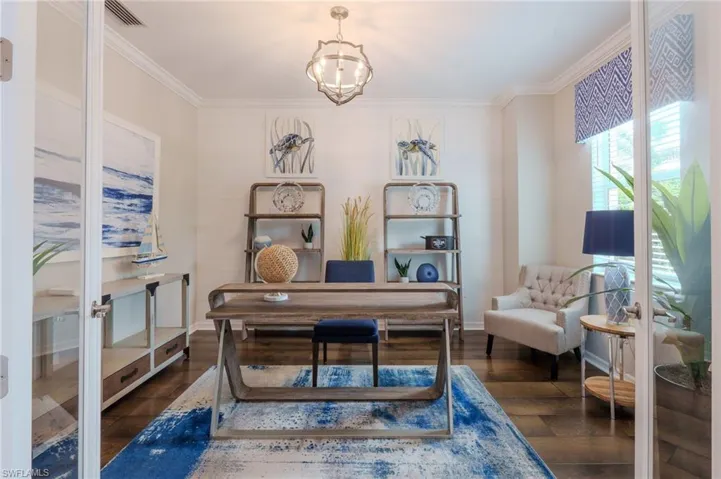 Dedicated room featuring double glass-paneled doors, rich wood-finish flooring, crown molding, and a contemporary light fixture