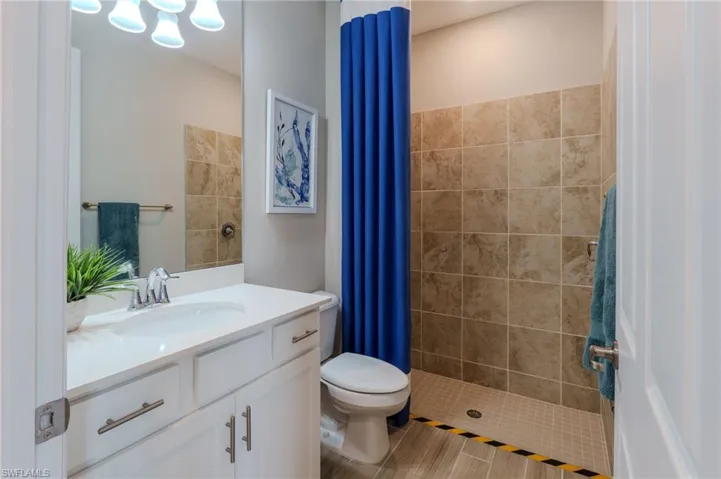 Bathroom featuring a walk-in shower with neutral-toned tile surround, a white vanity with integrated sink, and a chrome faucet