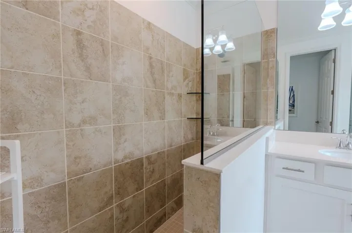 Tiled shower with glass partition, built-in shelving, and a vanity with a white countertop