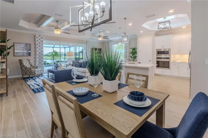 Open-concept living area featuring wood-finish flooring, a contemporary dining space, and a kitchen with white cabinetry and stainless steel appliances
