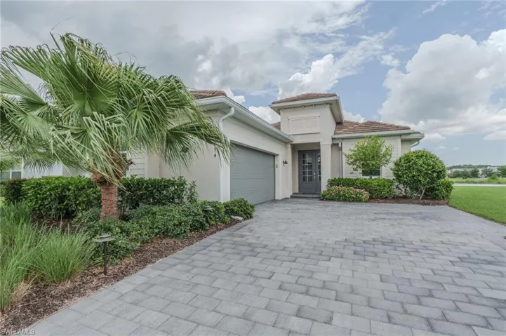Stucco exterior with a tile roof, an integrated garage, a paver driveway, and mature landscaping