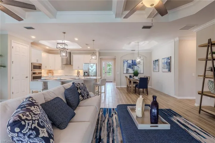 Open-concept living space featuring wood-finish flooring, a coffered ceiling, and a kitchen with white cabinetry and stainless steel appliances