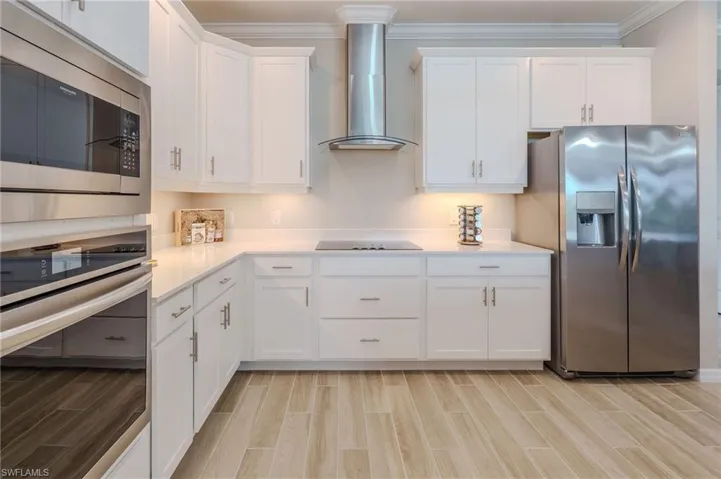 Modern kitchen featuring a stainless steel appliance suite, white cabinetry with brushed nickel hardware, and light-toned wood-finish flooring