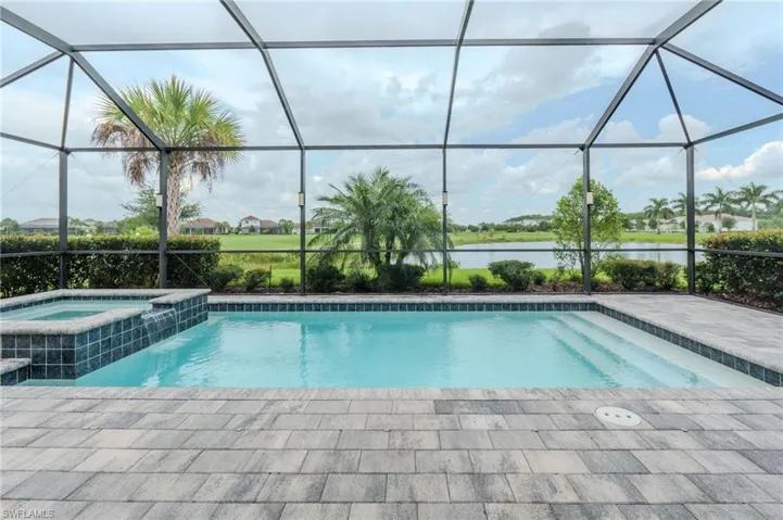 Screened outdoor living area featuring a rectangular pool and integrated spa with a waterfall feature