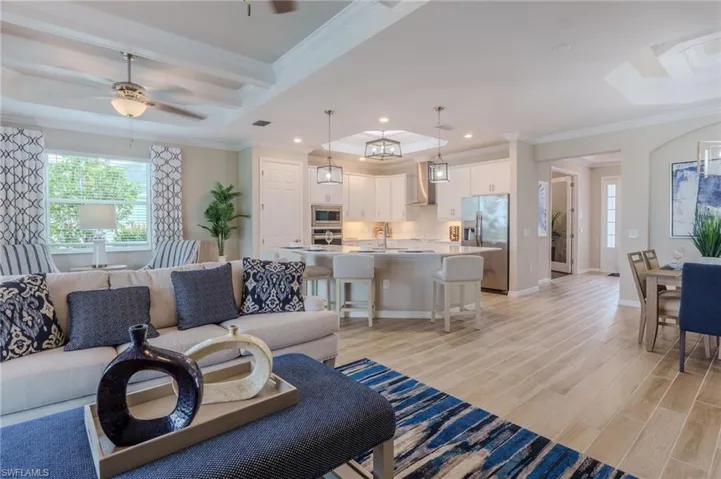 Open-concept living area featuring wood-finish flooring, a contemporary kitchen with white cabinetry and stainless steel appliances, a dining area, and a coffered ceiling