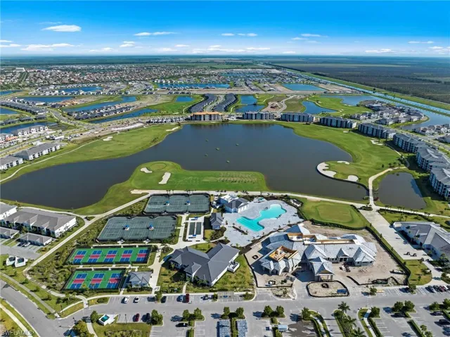 Aerial overview featuring a large central lake, surrounding golf course, multiple tennis courts, pickleball courts, and a resort-style swimming pool