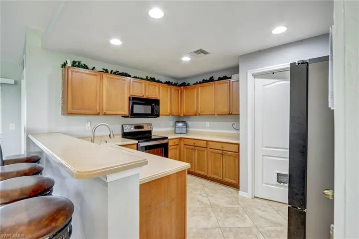 Kitchen with freestanding refrigerator, stainless steel range with electric stovetop, light countertops, black microwave, and a peninsula